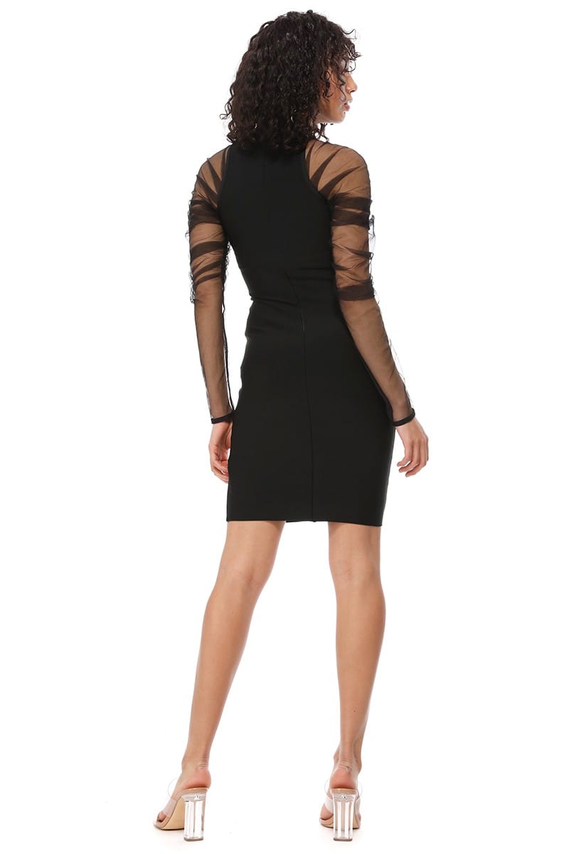 A woman shown from the back wearing a black bodycon mini dress with sheer mesh sleeves and crisscross strap detailing on the shoulders, paired with clear high-heeled sandals against a white background.