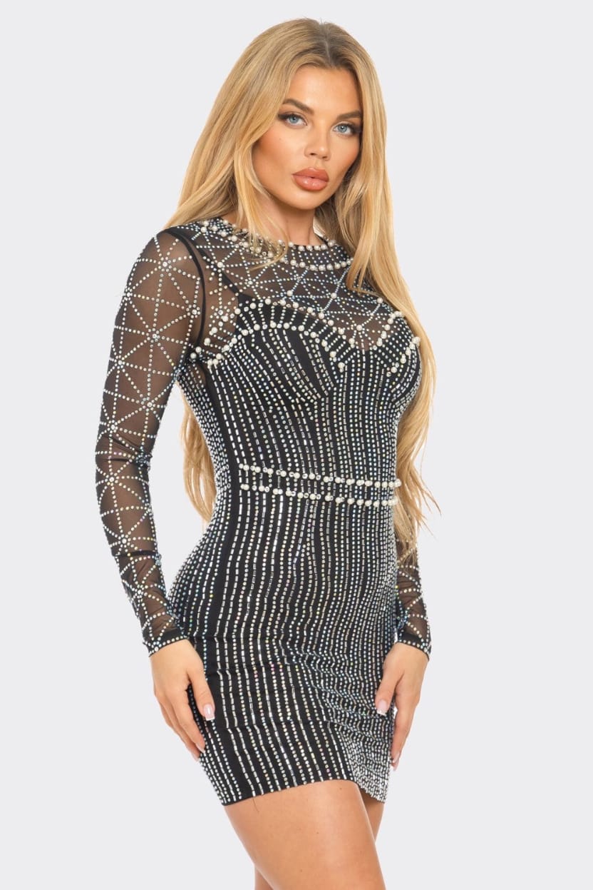 A blonde model wearing a black long-sleeve mini dress covered in intricate silver rhinestone beadwork, set against a solid light gray background.