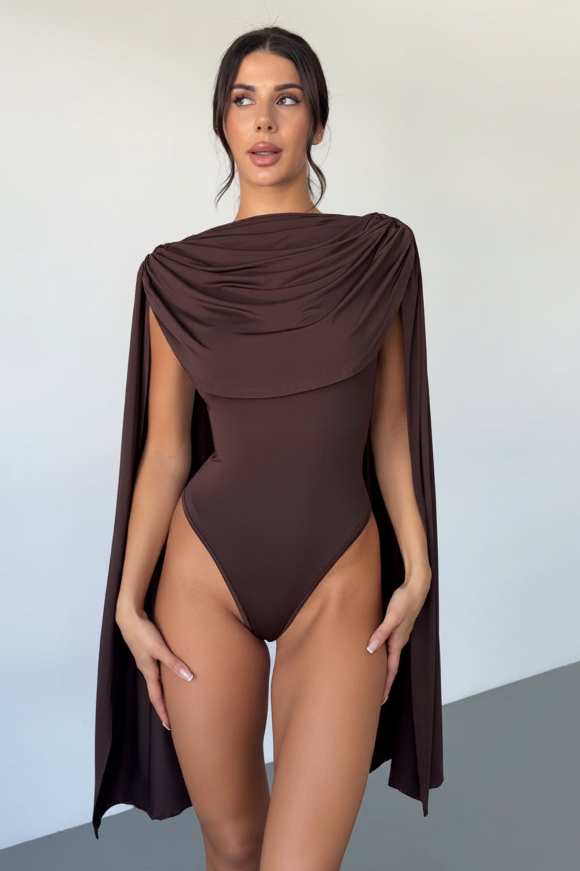 Woman wearing a brown one-piece swimsuit with cape-like design against a plain background