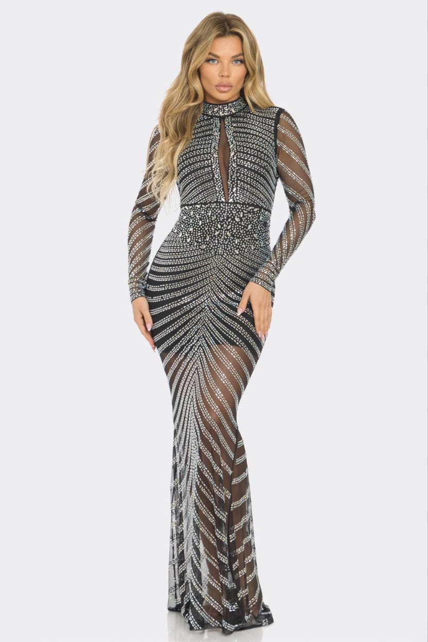 A woman modeling a long-sleeve, high-neck, floor-length gown covered in silver and black beaded geometric patterns over sheer mesh fabric, set against a plain light gray background.