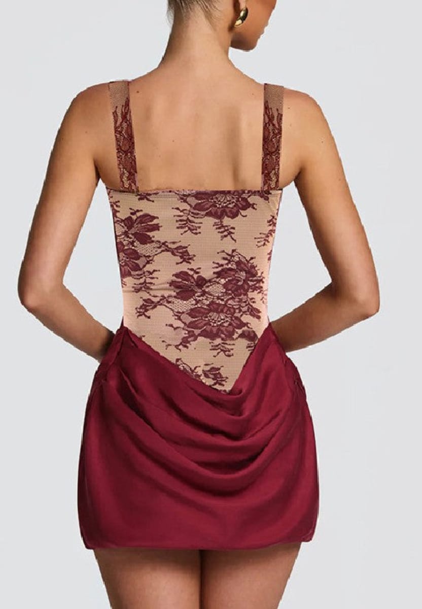 Rear view of a model wearing a short dress with a beige floral lace bodice and a draped burgundy skirt, set against a solid light gray background.