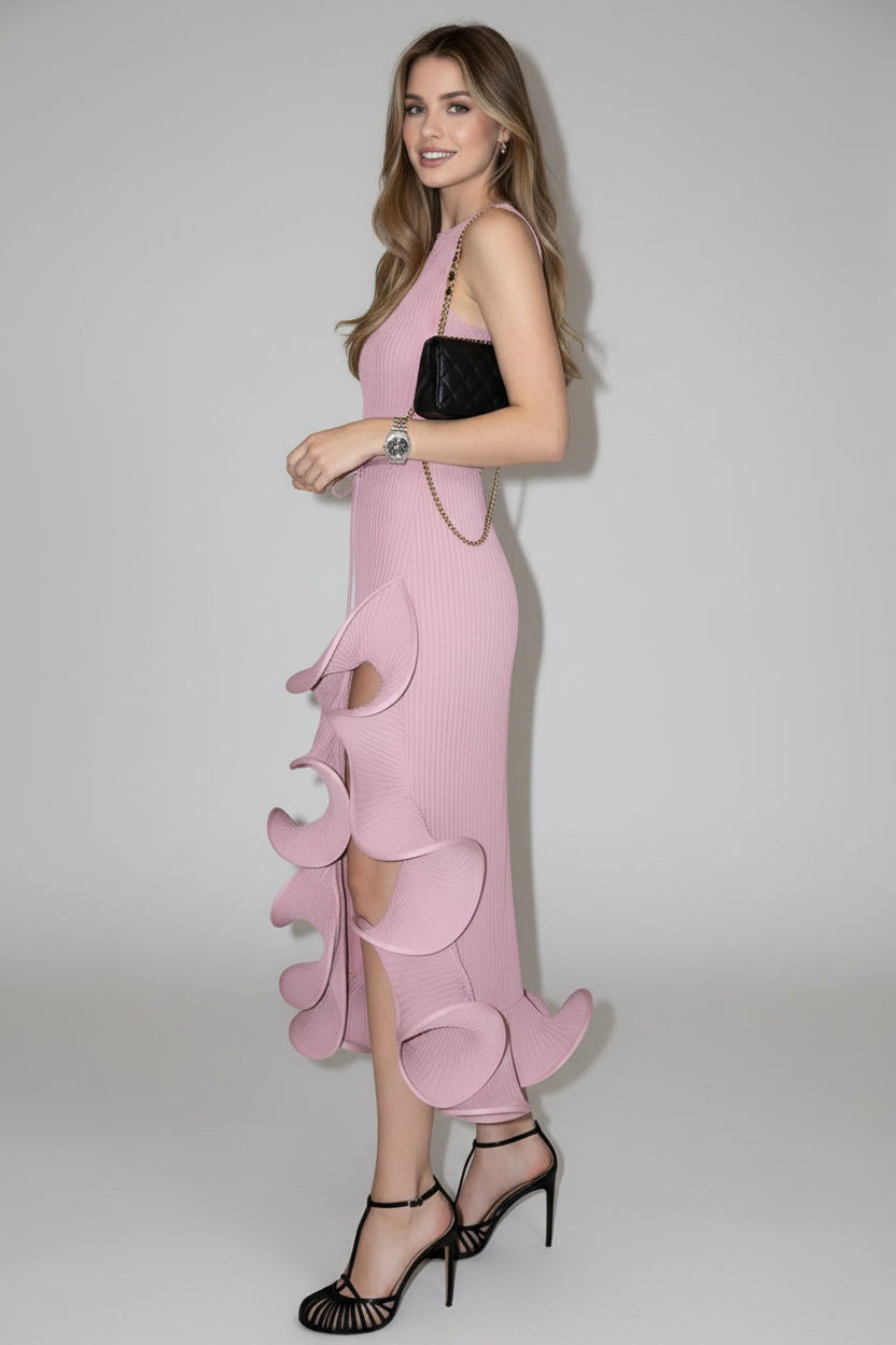 Woman wearing a pink dress with ruffled details against a white wall.