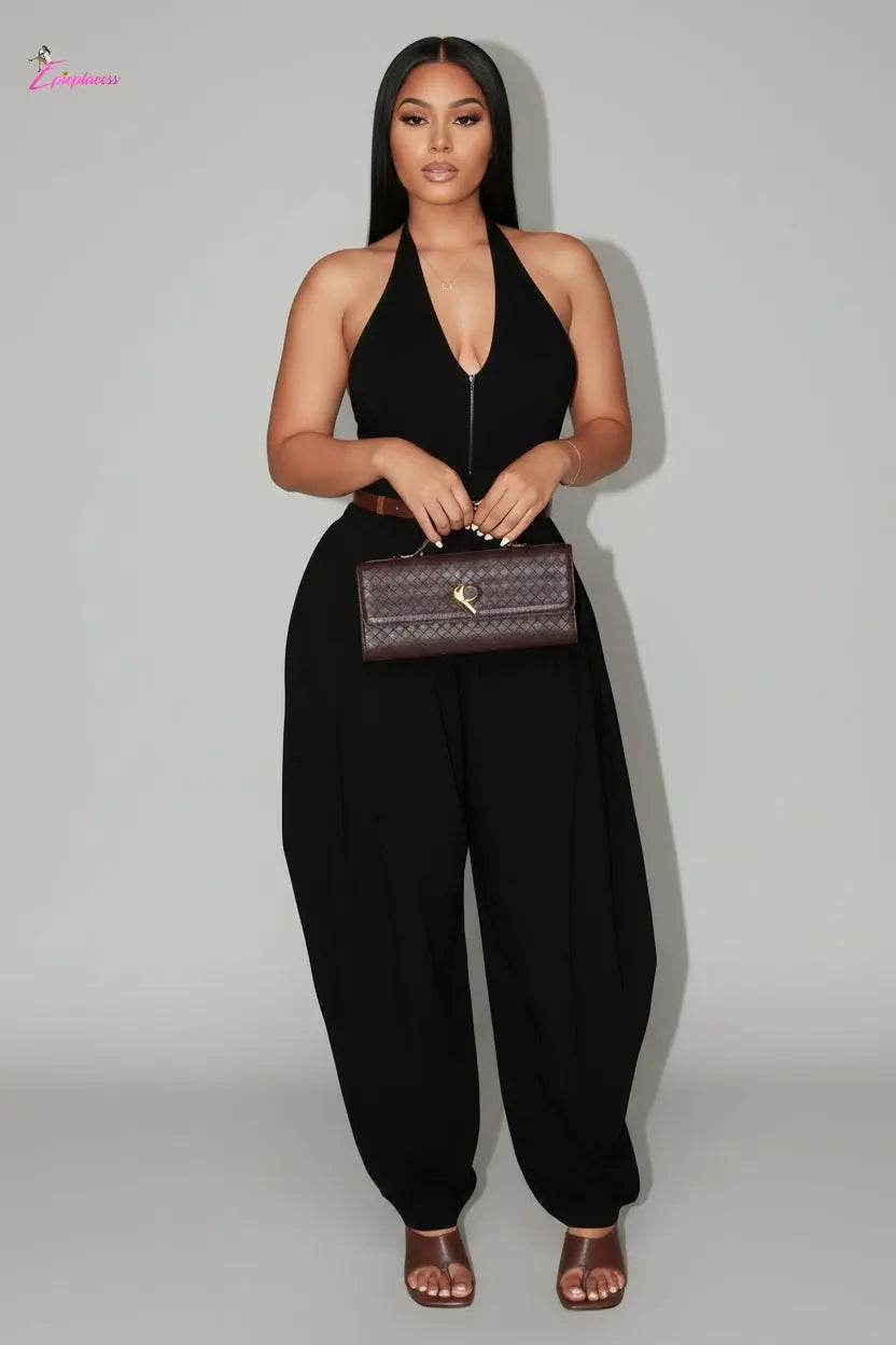 Woman in a black dress holding a brown clutch against a gray wall.