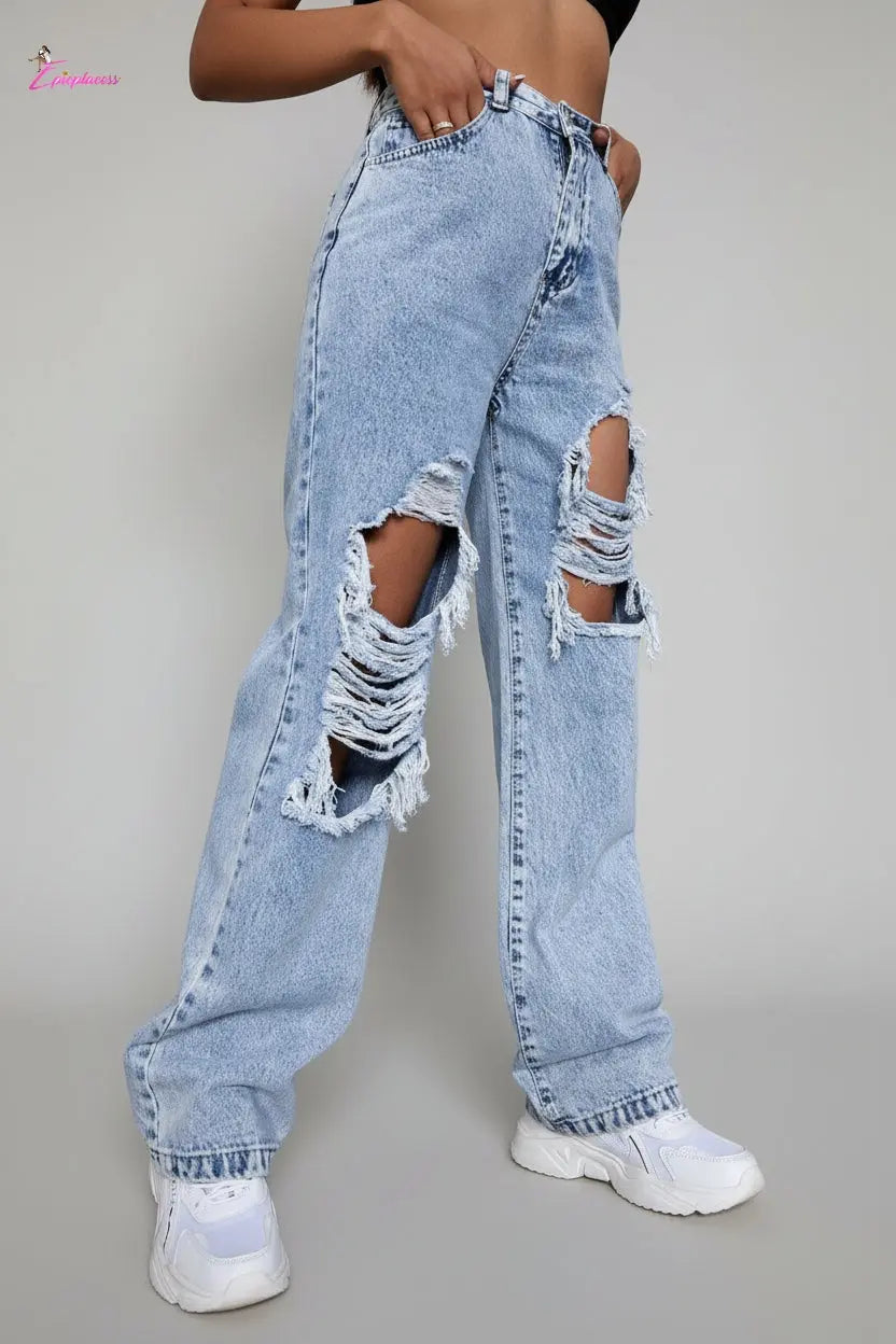 Person wearing ripped light blue jeans against a concrete wall.