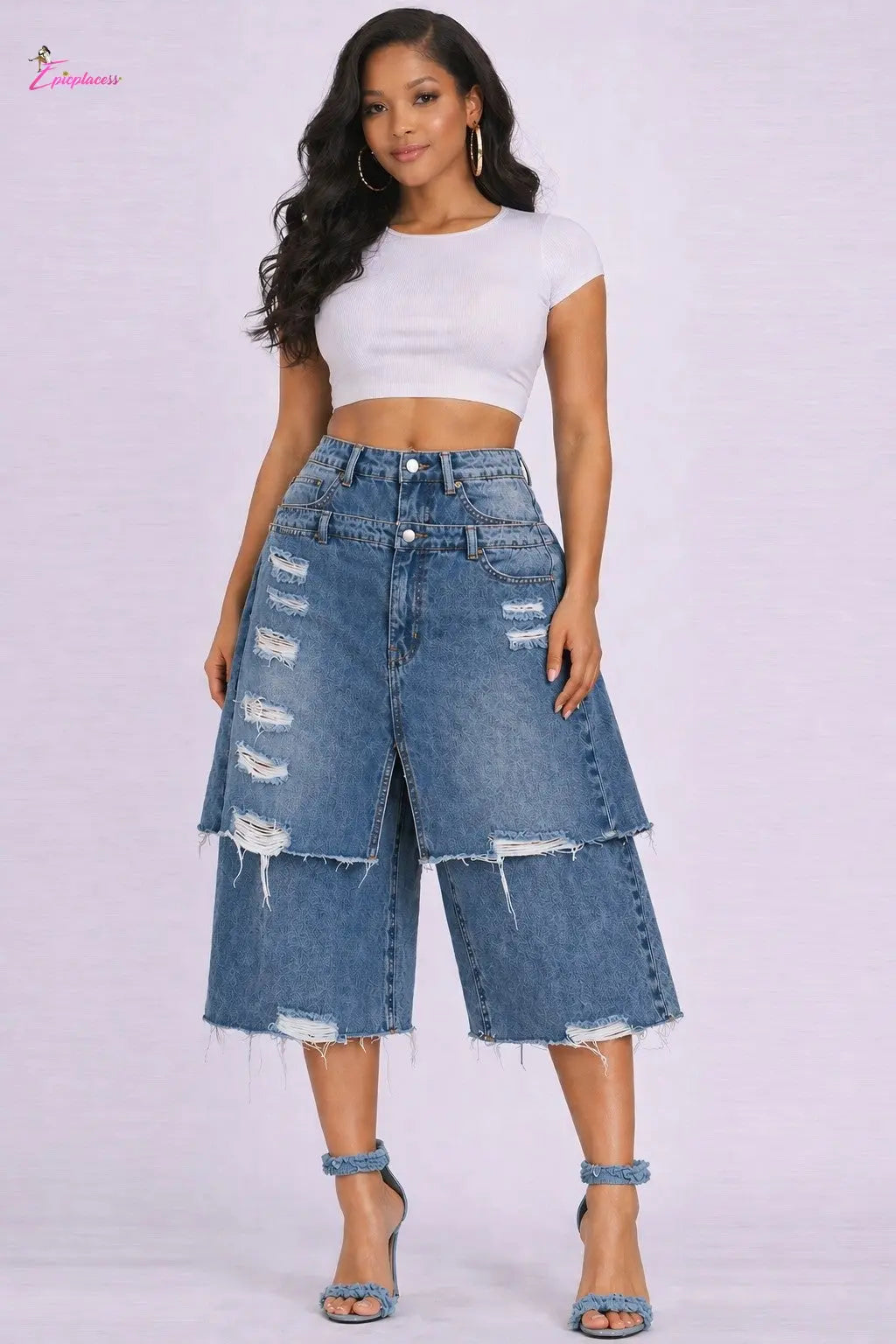 Woman wearing a white crop top and distressed denim shorts on a light purple background
