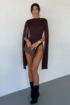 Woman wearing a brown caped outfit with black boots against a white background