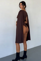 Woman wearing a brown cape over a revealing outfit against a white background