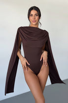 Woman wearing a brown swimsuit with a cape-like design against a plain background