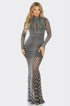 A woman modeling a long-sleeve, high-neck, floor-length gown covered in silver and black beaded geometric patterns over sheer mesh fabric, set against a plain light gray background.