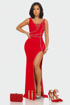 A woman modeling a bright red sleeveless maxi gown with a high thigh slit, embellished with silver chain details and a jeweled neckline, set against a plain light gray background.