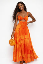 Woman wearing an orange floral dress holding a matching handbag against a white background