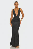 A woman modeling a dark charcoal gray sleeveless maxi dress with a plunging V-neckline, side cutouts, and a fitted mermaid silhouette against a light gray studio background.