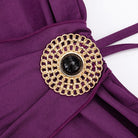 Close-up of a purple garment with a gold and black decorative brooch on a white background