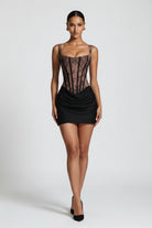 A model wearing a black and sheer brown lace mini dress with a corset-style bodice and ruched skirt, shown against a light gray studio background.