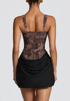A model shown from the back wearing a black and brown floral lace mini dress with a ruched black skirt against a light gray background.