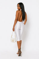 Woman wearing a white outfit with a backless design, holding a white handbag against a white background.