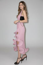 Woman wearing a pink dress with ruffled details against a white wall.