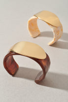 Two gold and tortoiseshell cuff bracelets on a beige background
