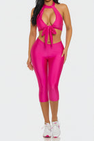 Woman wearing a bright pink outfit with a halter top and capri pants on a white background