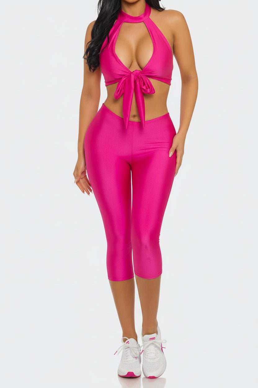 Woman wearing a bright pink outfit with a halter top and capri pants on a white background