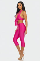 Woman wearing a bright pink outfit with a halter top and leggings on a white background