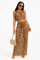 Woman wearing a gold sequin outfit with sunglasses and a handbag on a white background