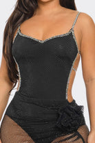 A close-up of a woman wearing a black mesh bodysuit with silver rhinestone trim along the straps and neckline, plus a matching black fishnet skirt with a ruffled overlay.
