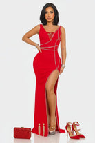 A woman modeling a bright red sleeveless maxi gown with a high thigh slit, embellished with silver chain details and a jeweled neckline, set against a plain light gray background.