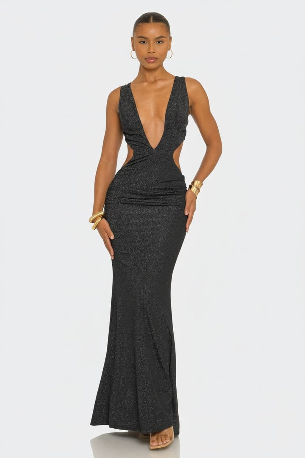 A woman modeling a dark charcoal gray sleeveless maxi dress with a plunging V-neckline, side cutouts, and a fitted mermaid silhouette against a light gray studio background.