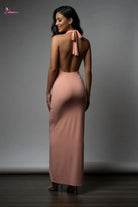 Woman wearing a long, light pink dress with a backless design against a gray background