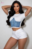 Woman wearing a white t-shirt with denim top and white shorts against a plain background
