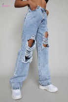 Person wearing ripped light blue jeans against a concrete wall.