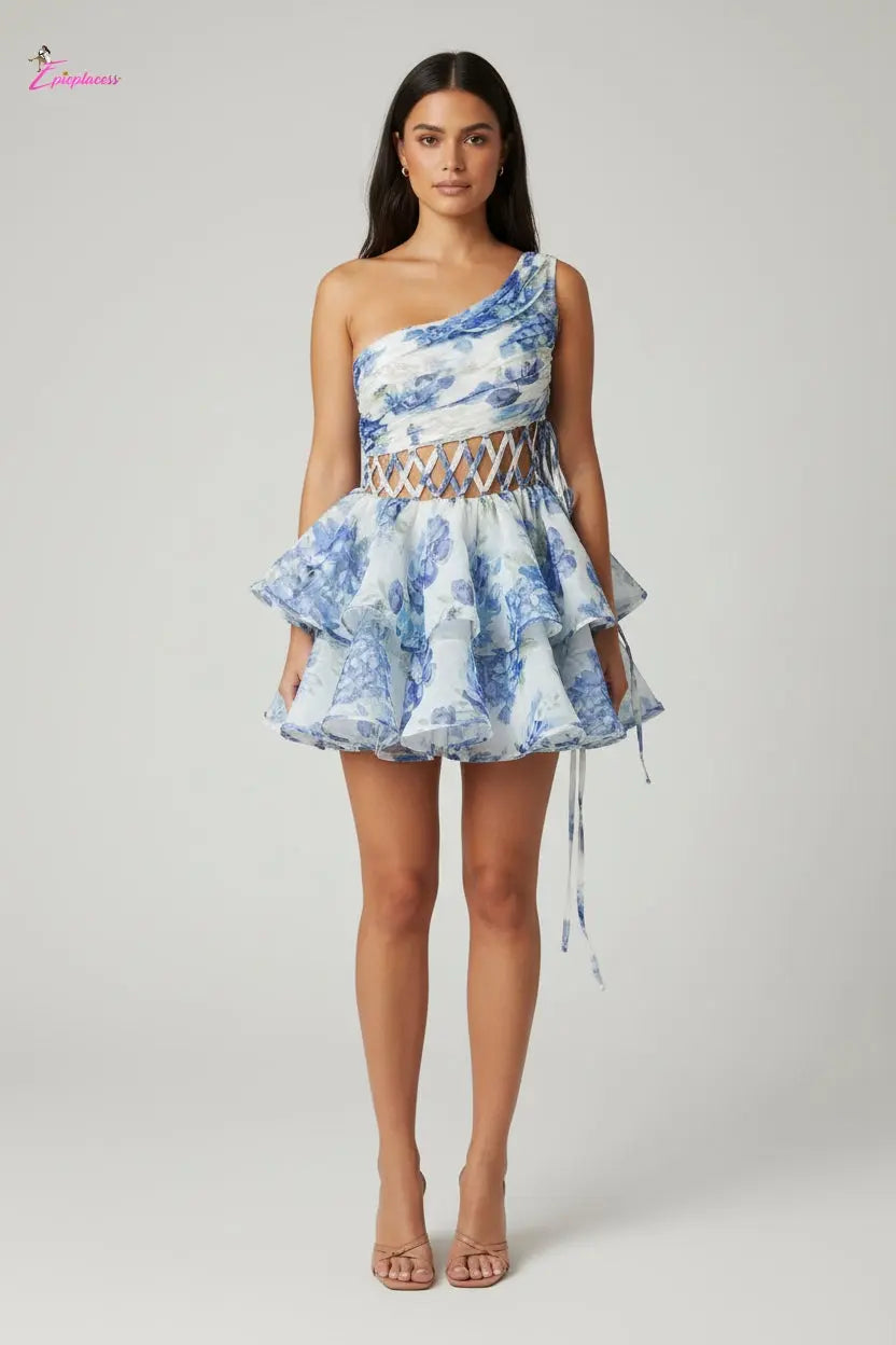 Woman wearing a blue floral dress standing against a wooden bench with greenery in the background.